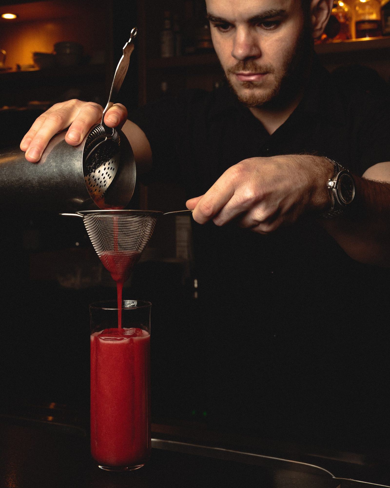 Le barman de Dario verse un cocktail au tamis dans la pénombre du bar