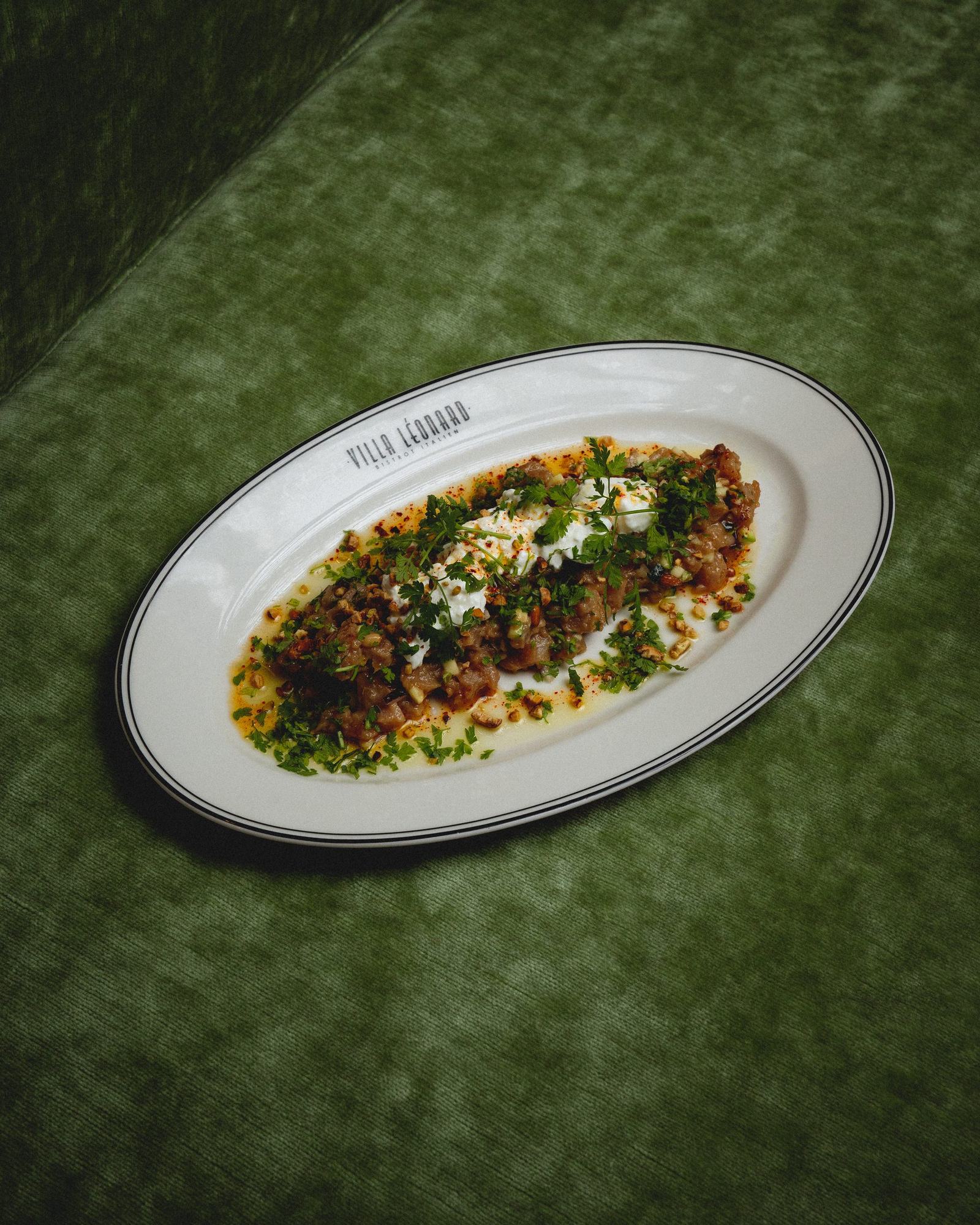 Un plat de la Villa Léonard dressé sur assiette ovale, posé sur le velours vert de la charte