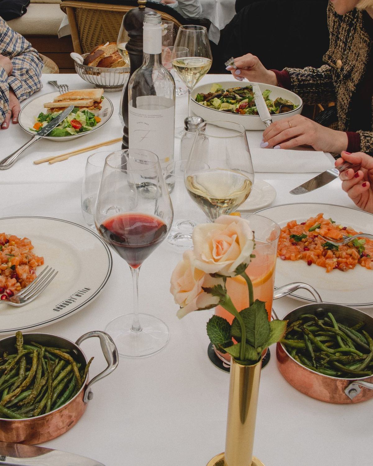 Une tablée à la Villa Léonard : assiettes partagées, roses et verres de vin sur nappe blanche